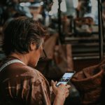 Mulher observa o celular em meio ao movimento de um mercado