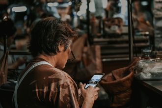 Mulher observa o celular em meio ao movimento de um mercado