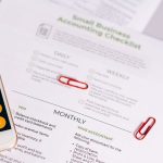 Checklist e calculadora sobre uma mesa, usados para organizar tarefas de contabilidade de um pequeno negócio.