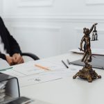 Mesa de trabalho jurídico com documentos, laptop e uma estátua da Justiça.