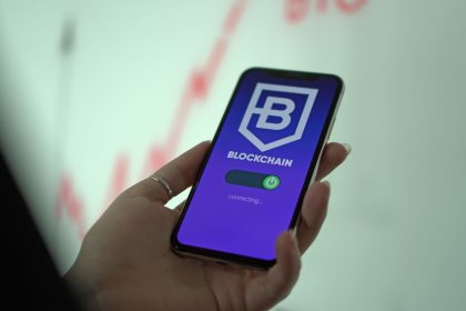 Mão segurando um smartphone que exibe uma carteira digital de criptomoedas e elementos de blockchain