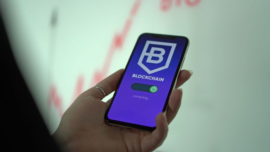 Mão segurando um smartphone que exibe uma carteira digital de criptomoedas e elementos de blockchain