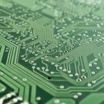 Close de uma placa de circuito impresso com trilhas, componentes eletrônicos e microprocessador.