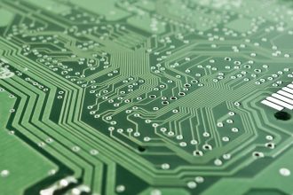 Close de uma placa de circuito impresso com trilhas, componentes eletrônicos e microprocessador.