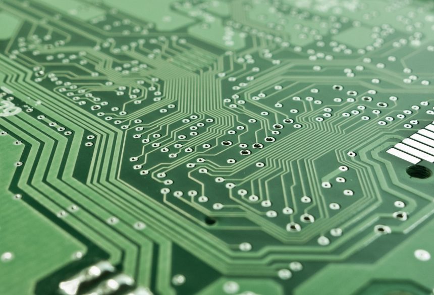 Close de uma placa de circuito impresso com trilhas, componentes eletrônicos e microprocessador.