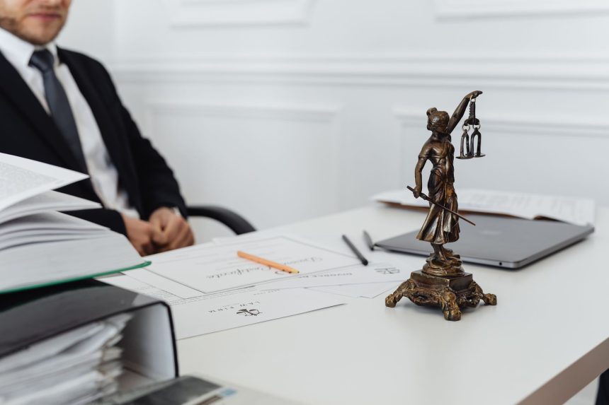 Mesa de trabalho jurídico com documentos, laptop e uma estátua da Justiça.